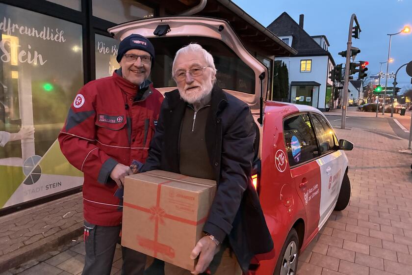 Ein Johanniter in roter Einsatzkleidung übergibt symbolisch ein Hilfspaket an den Vertreter der Steiner Tafel.