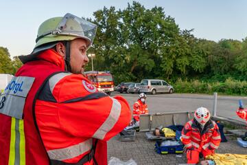 Ein Einsatzleiter der Johanniter gibt Anweisungen, während im Hintergrund Sanitäter*innen Verletzte versorgen.