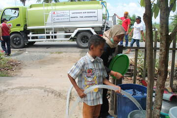 Ein kleiner Junge füllt ein Fass mit Trinkwagen aus einem Tanklaster von INANTA