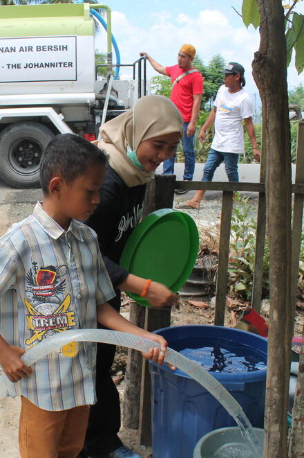 Ein kleiner Junge füllt ein Fass mit Trinkwagen aus einem Tanklaster von INANTA