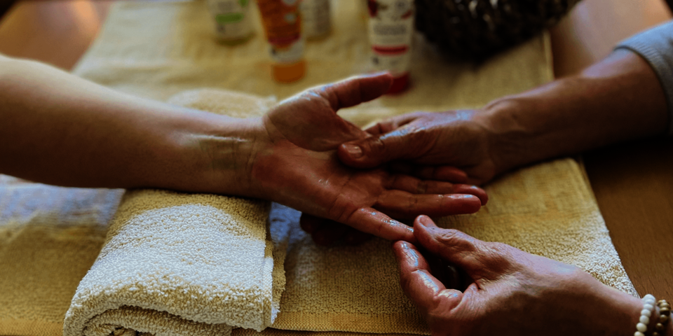 ein Hand liegt auf einem gerollten Handtuch und wird von zwei weiteren Händen massiert.