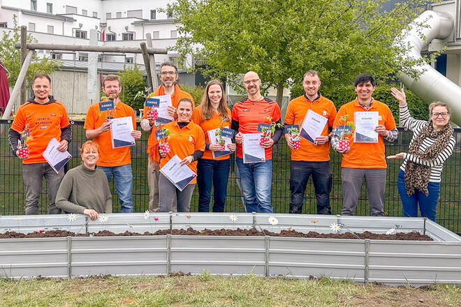 Mehrere Sixt Mitarbeiter stehen vor einem Blumenbeet und halten Urkunden in der Hand.