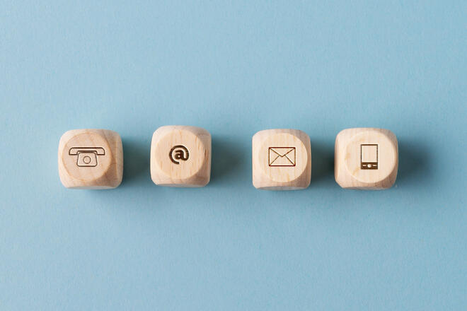 Vier Holzklötze mit Symbolen für Telefon, E-Mail und Smartphone auf blauem Hintergrund.