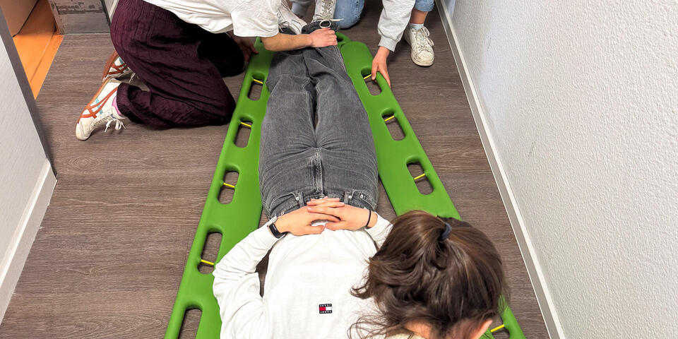 Eine Person wird von Helfenden in einer Schaufeltrage fixiert