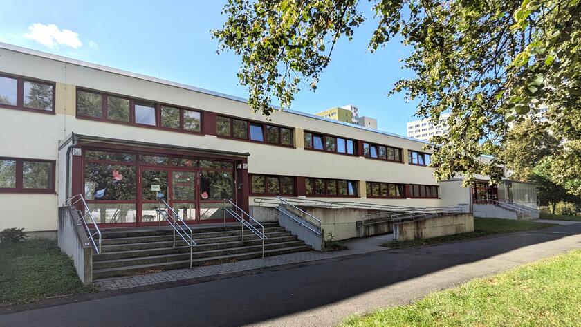 Das Gebäude der Kindertagesstätte mit Treppenaufgang, davor befindet sich ein Fußweg sowie eine Grünfläche.