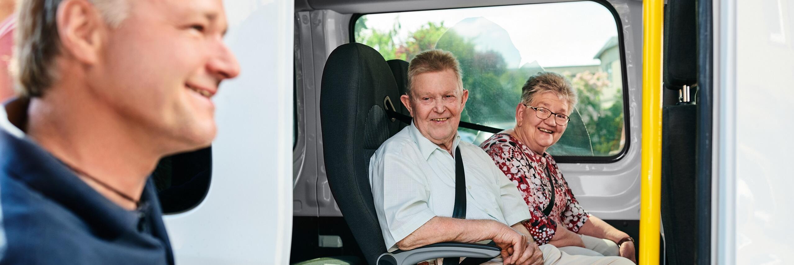 Zwei Personen sitzen in einem Auto, der Fahrer öffnet die Tür