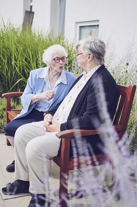 Zwei Bewohner genießen die frische Luft und sitzen auf einer Bank