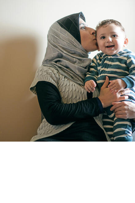 Eine Frau mit Kopftuch küsst ein lachendes Kleinkind.