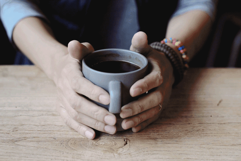 Hände umfassen eine Tasse Kaffee.