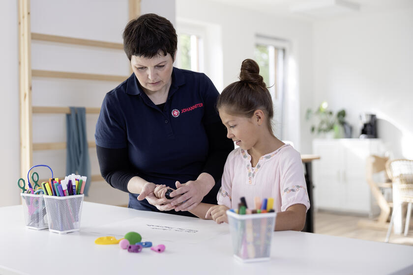 Eine Ergotherapeutin führt mit einem Kind eine ergotherapeutische Übung mit einem Igelball durch.