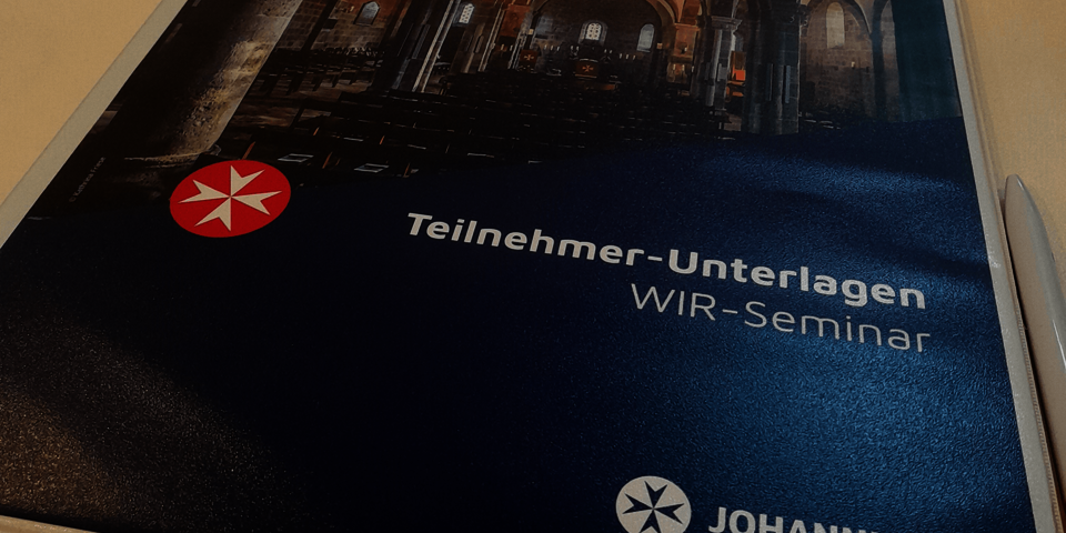 Teil einer Broschüre, darauf ein weißes achtspitziges Kreuz auf rotem kreis als Bildmarke der johanniter und die Aufschrift "Teilnehmer-Unterlagen WIR-Seminar"
