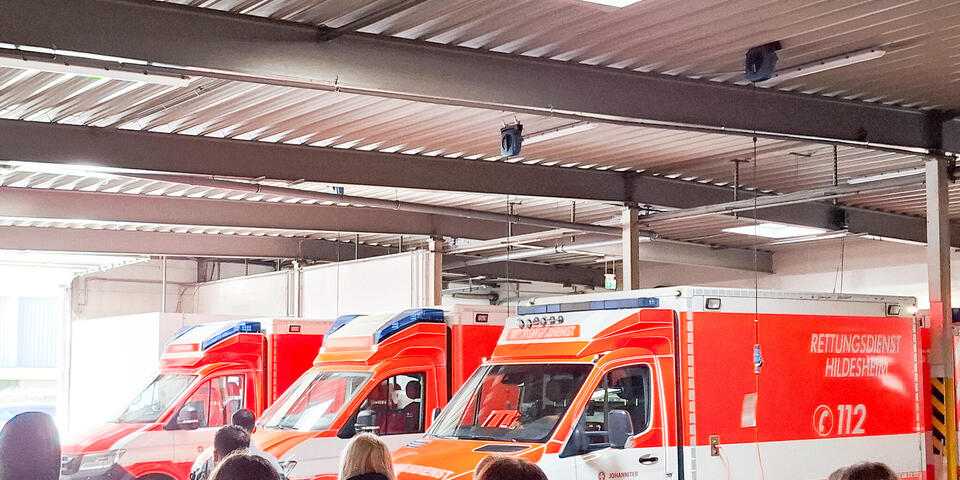 Junge Menschen in einer Fahrzeughalle. Im Hintergrund mehrere RTWs