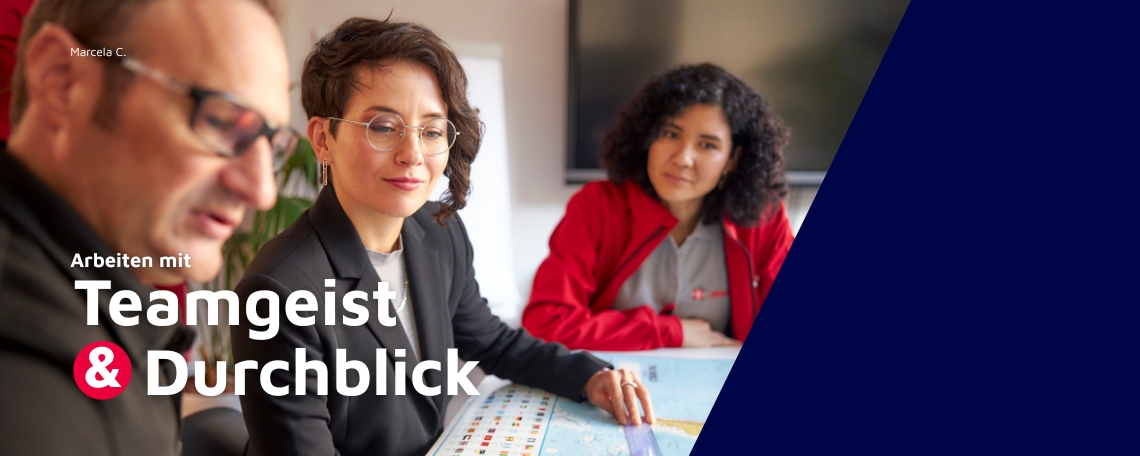Drei Personen sitzen an einem Tisch und blicken konzentriert auf einen Stadtplan oder eine Karte. Im Vordergrund links ist ein Mann leicht unscharf zu sehen, daneben sitzt Marcella C. (Teamassistenz) mit Brille und kurzem Haar, die aufmerksam zuhört. Im H